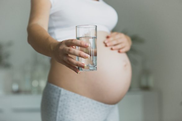 Mulher grávida, com a mão na barriga segurando um copo de água